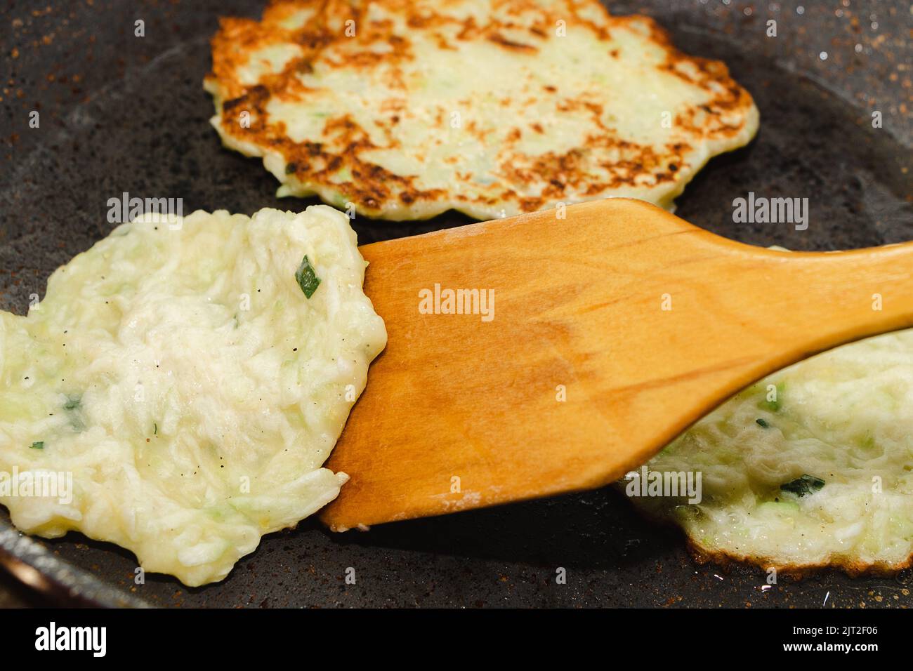 Rezept für Zucchini-Krapfen. Schritt 5 - Pfannkuchen in der Pfanne goldbraun braten. Pfannkuchen mit Holzspachtel umschlagen. Stockfoto