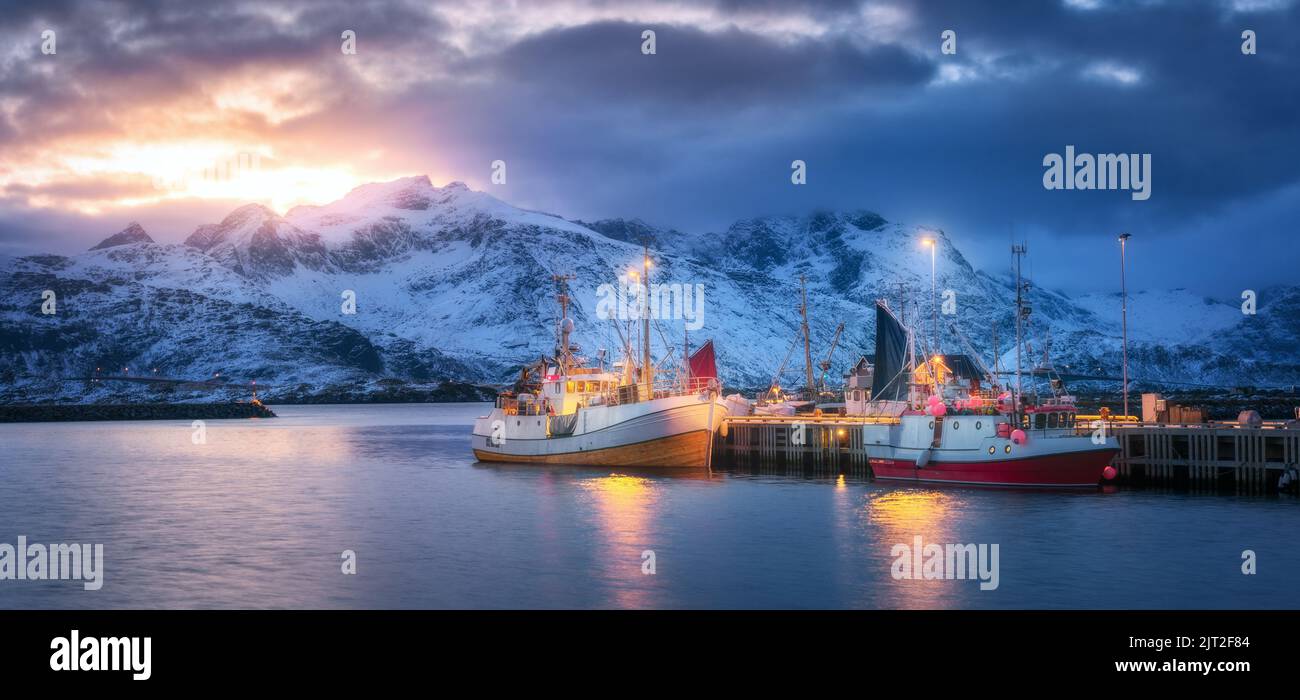 Fischerboote auf dem Meer, verschneite Berge, farbenfroher Himmel Stockfoto