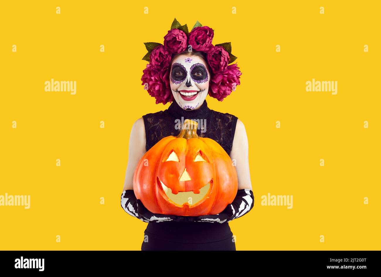 Fröhliche Frau mit kreativem traditionellen mexikanischen Make-up mit leuchtendem Halloween-Kürbis. Stockfoto