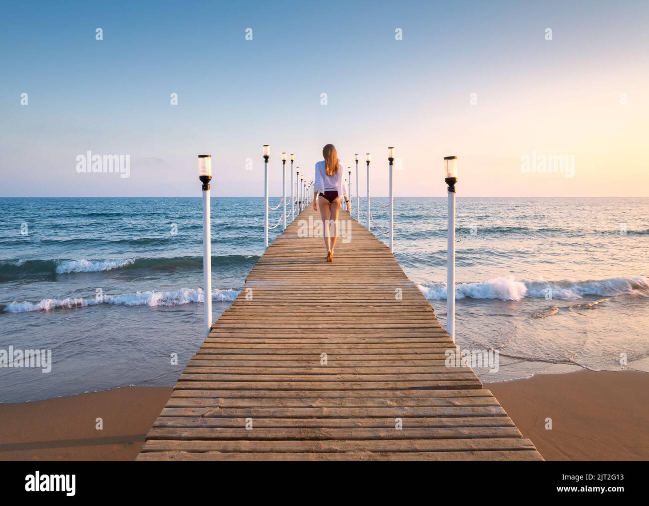 Glückliche junge Frau im Bikini, die auf dem hölzernen Pier am Meer läuft Stockfoto