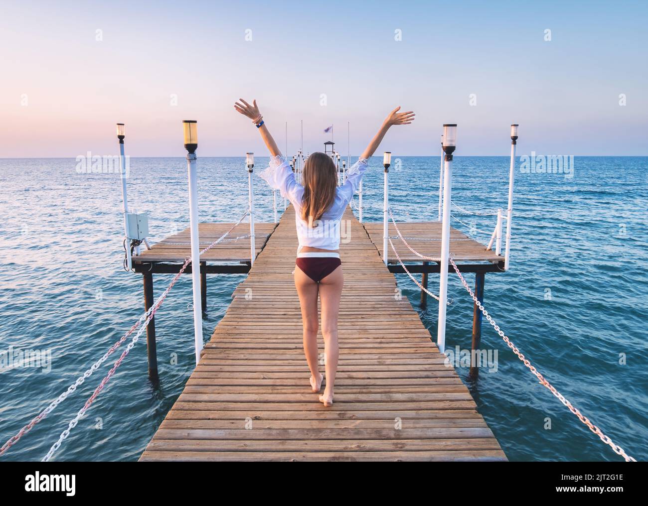 Glückliche junge Frau im Bikini mit erhobenen Armen auf dem Pier zu Fuß Stockfoto