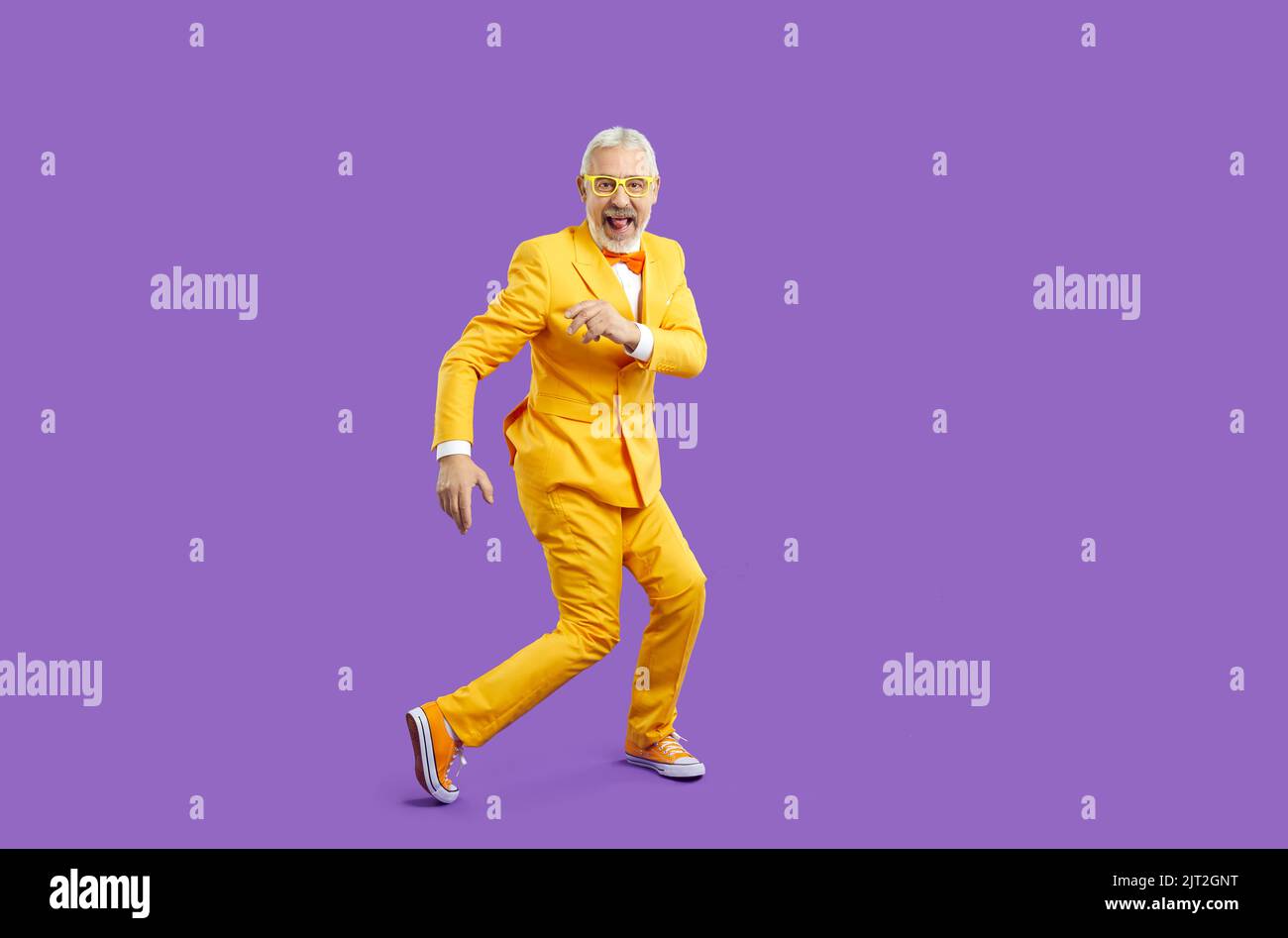 Fröhlich trendy, exzentrisch und energisch Senior Mann lustig tanzen isoliert auf lila Hintergrund. Stockfoto