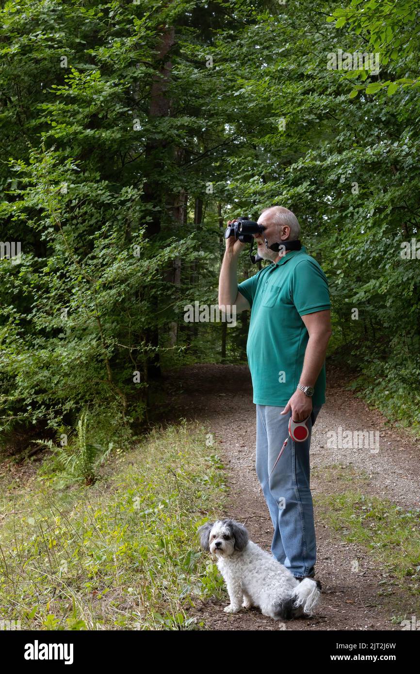 Der Mensch beobachtet die Natur mit einem Fernglas, während sein Hund sitzt Stockfoto