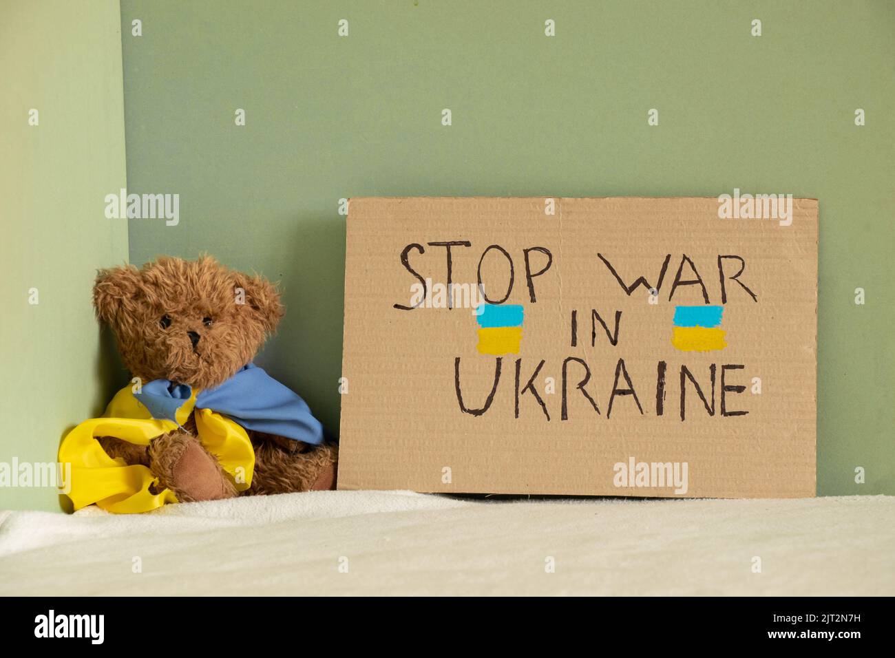 Stoppt den Krieg in der Ukraine, geschrieben auf einem Schild, das auf dem Bett eines Hauses in der Ukraine neben einem Teddybären steht. Frieden in der Ukraine. Protest 2022 Stockfoto