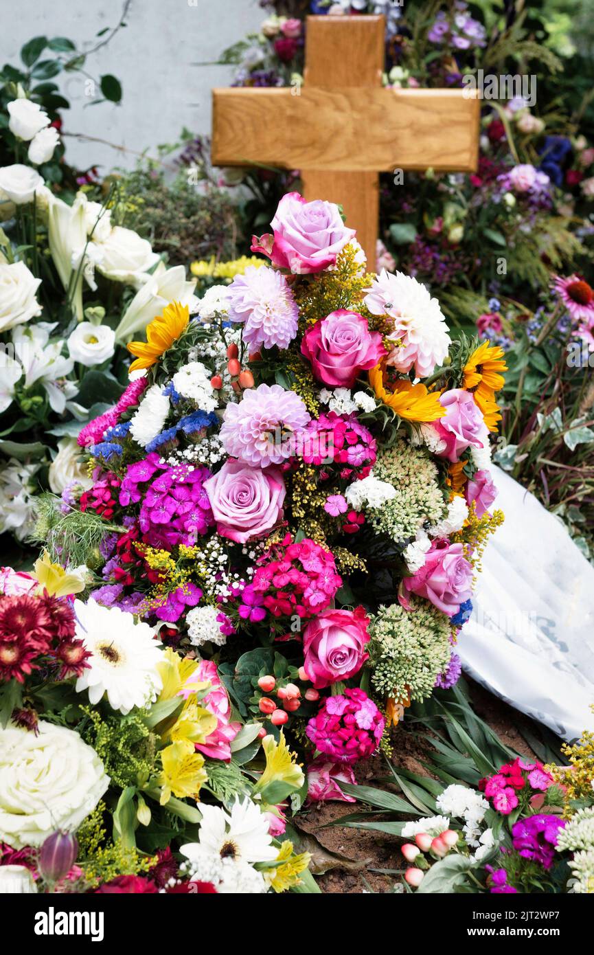 Bunte Blumen auf einem Grab mit einem Holzkreuz nach einer Beerdigung Stockfoto