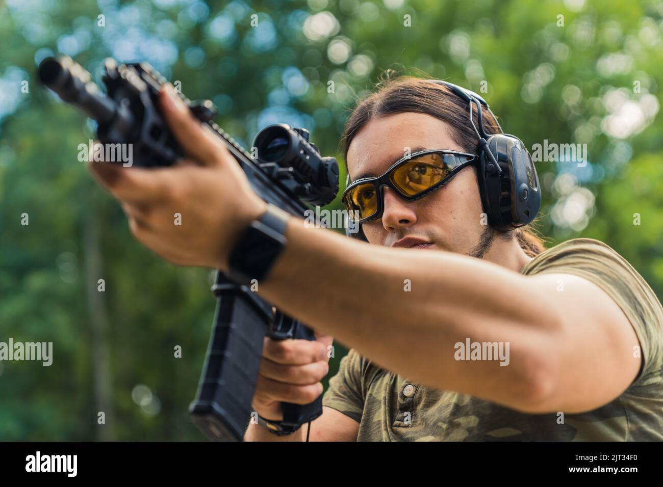 Nahaufnahme im Freien Porträt eines europäischen Mannes mittleren Alters in einer Schutzbrille und einem Kopfhörer, der dank der Lupe auf seinem Gewehr auf das Ziel zielt. Hochwertige Fotos Stockfoto