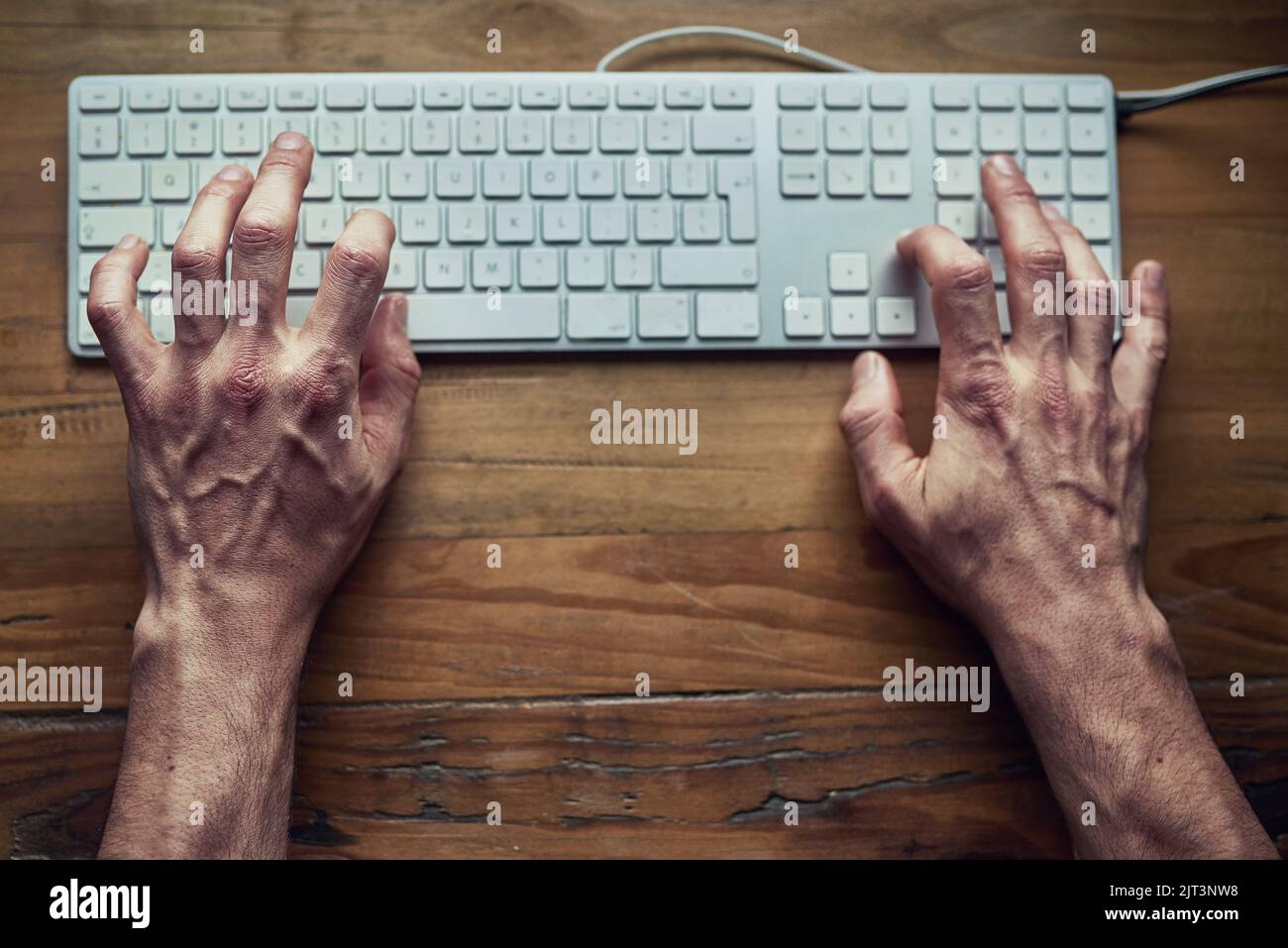 Eine schnelle Antwort auf eine E-Mail wird ausgelöst. High-Angle-Aufnahme eines nicht identifizierbaren Mannes, der nachts auf einer Computertastatur tippt. Stockfoto