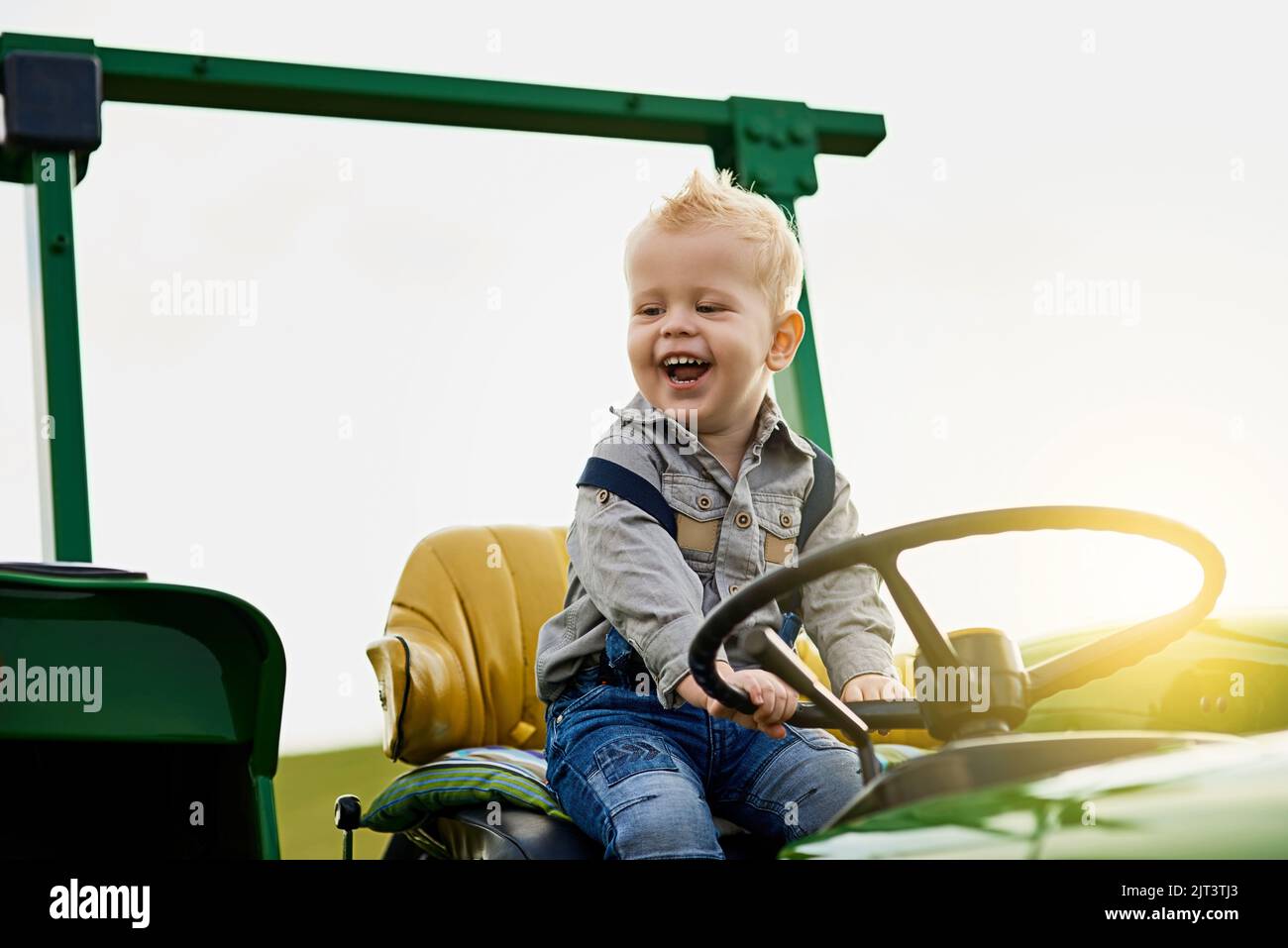 Jede Menge Spaß auf den Feldern. Ein entzückender kleiner Junge, der auf einem Traktor auf einer Farm reitet. Stockfoto