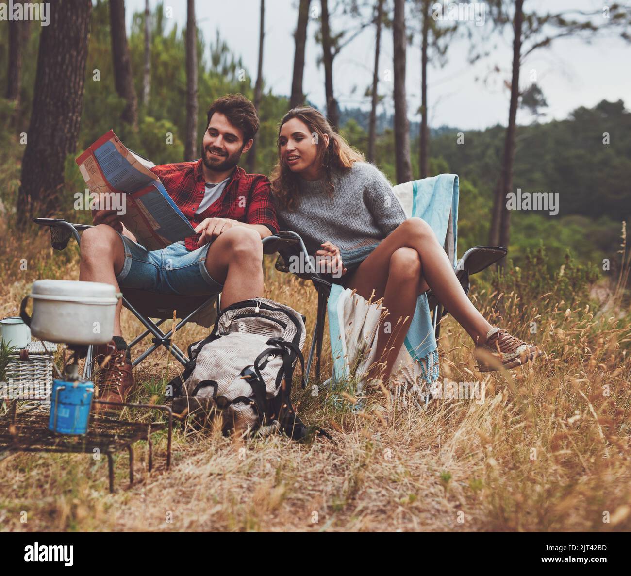 Abenteuerlustiges junges Paar, das sich auf einem Stadtplan ansieht, während es auf ihrem Campingplatz sitzt. Glückliches junges Paar, das im Wald zeltet. Stockfoto