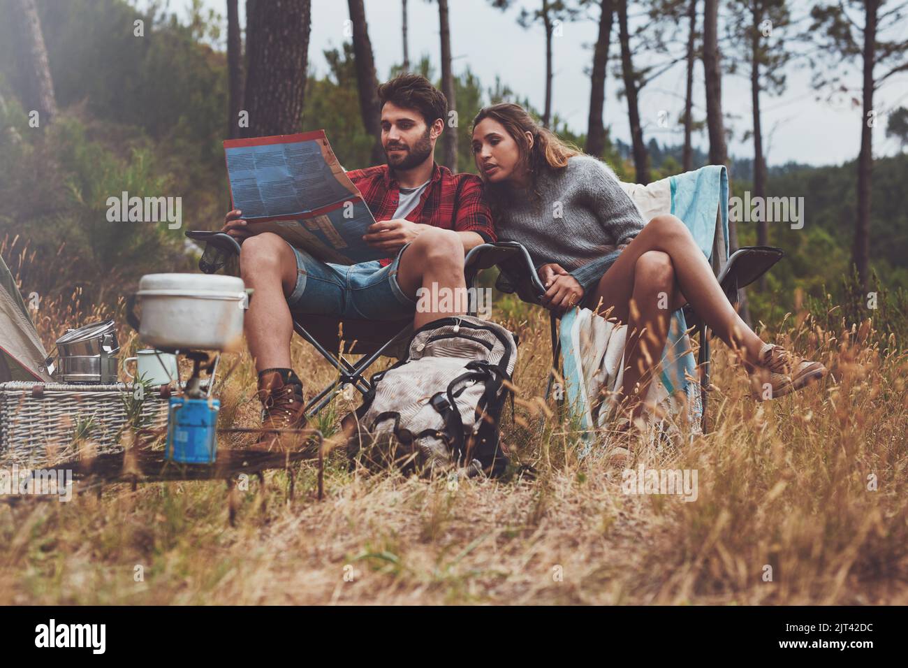 Junges Paar, das sich auf einem Stadtplan ansieht, während es auf seinem Campingplatz sitzt. Abenteuerliches junges Paar, das im Wald zeltet. Stockfoto