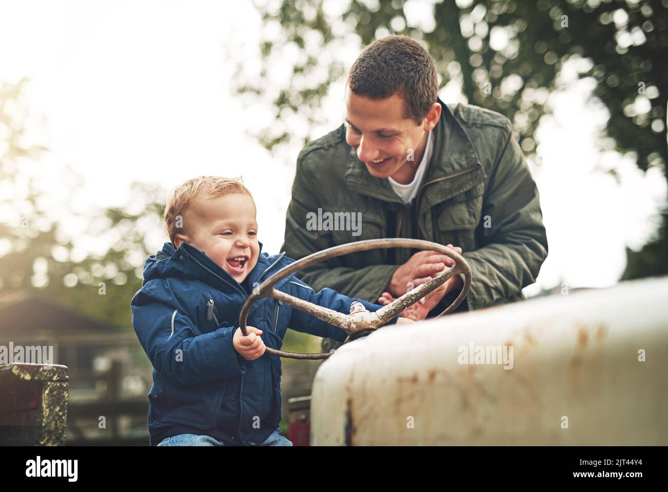 Die Kinder sind voller Neugier. Ein Vater und sein kleiner Sohn spielen draußen auf einem Traktor auf dem Bauernhof zusammen. Stockfoto
