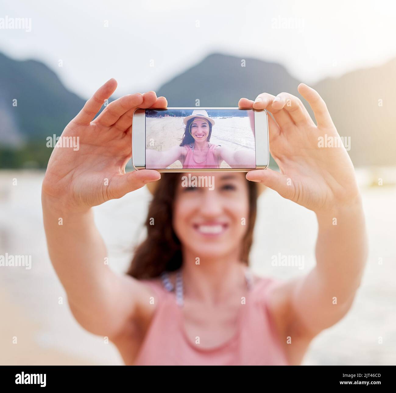 Schauen Sie, wo ich bin. Eine glückliche junge Frau, die ein Selfie mit ihrem Telefon an einem tropischen Strand macht. Stockfoto