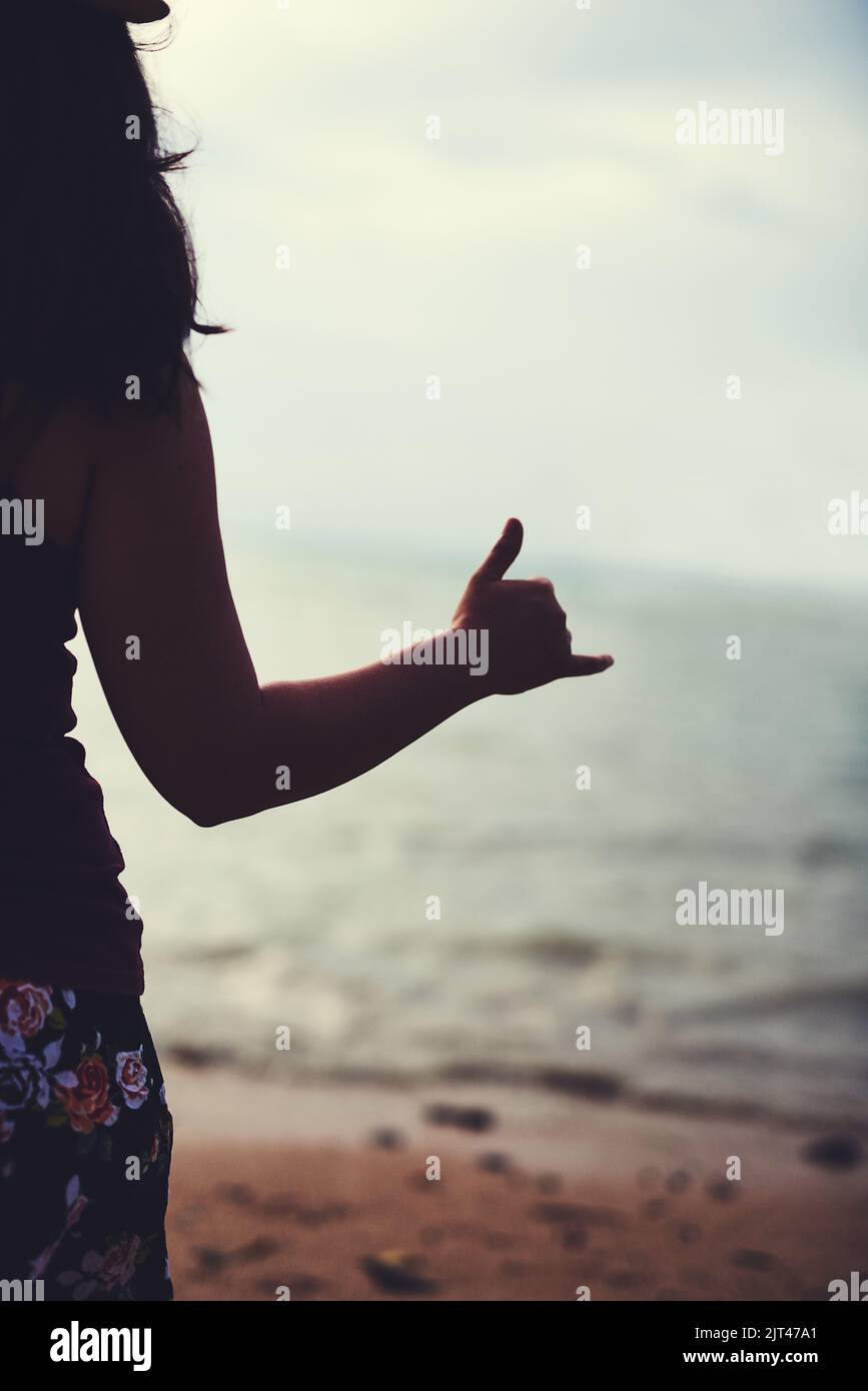 Surft auf. Rückansicht einer jungen Frau am Strand, gestikulend Hang Ten. Stockfoto