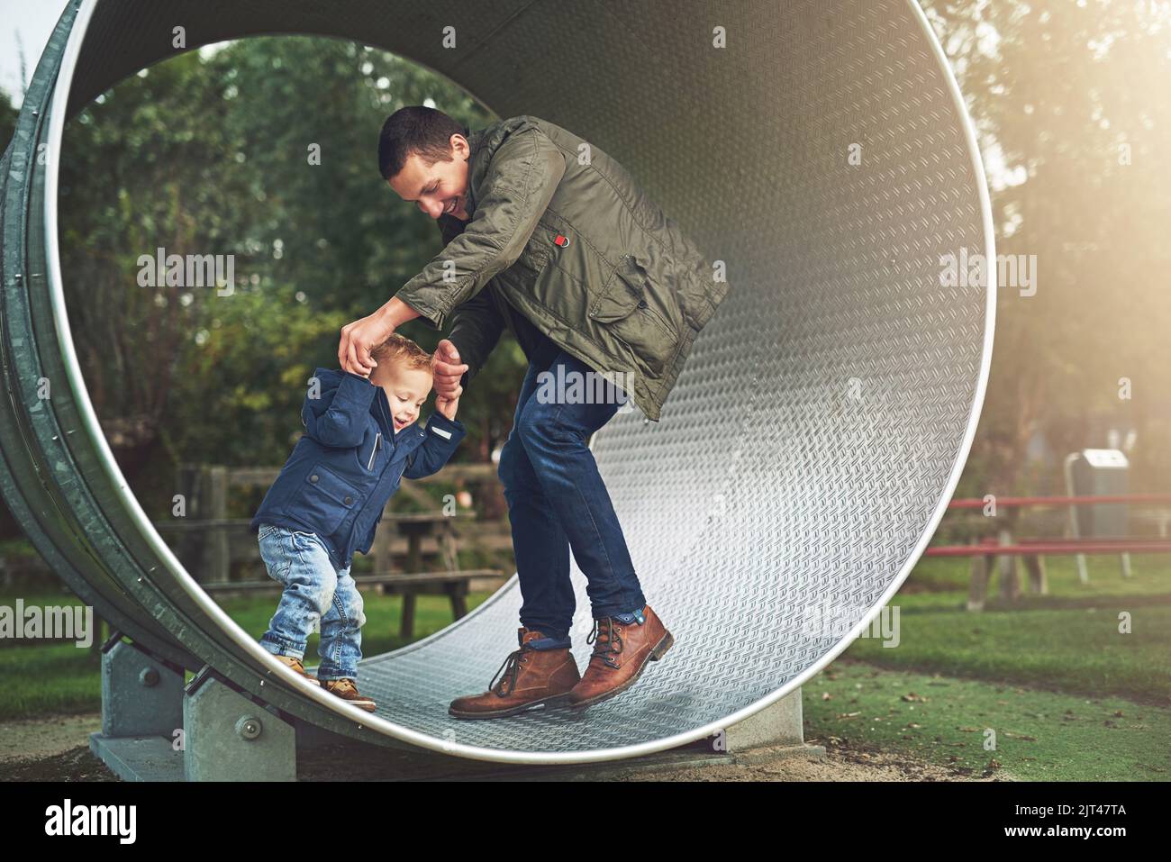 Versuchen Sie nicht zu fallen. Ein Vater und sein kleiner Sohn spielen zusammen auf einem Laufrad im Park. Stockfoto