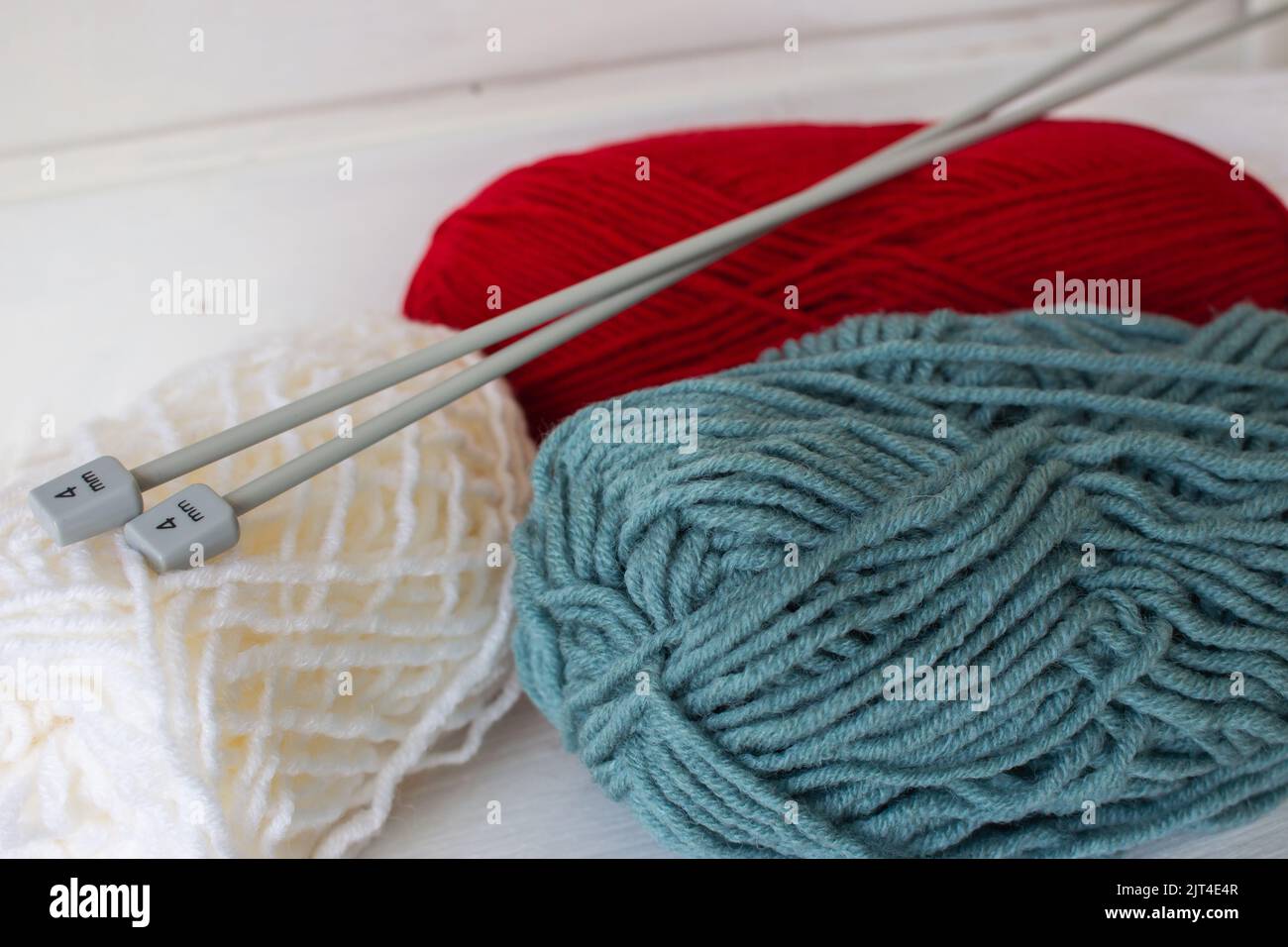 Bunte Strickgarne und Stricknadeln 4 mm. Weiße, rote und grüne warme Fadenrolle. Strickhobby. Nadelarbeitskonzept. Winter-Freizeitkonzept. Stockfoto