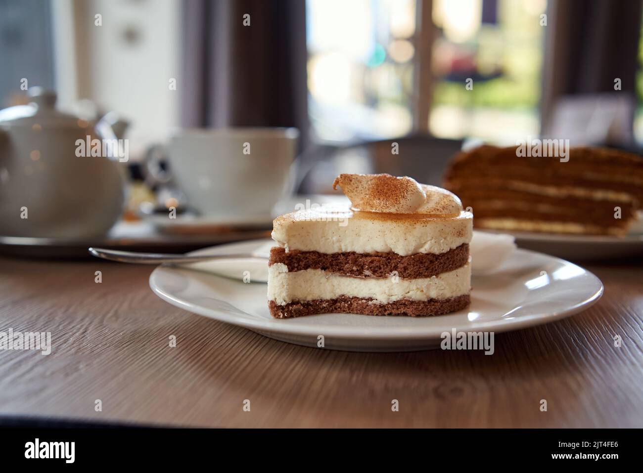 Leckerer Kuchen mit Mascarpone auf einem Tisch in einem Café, mit einer Tasse Tee im Hintergrund Stockfoto