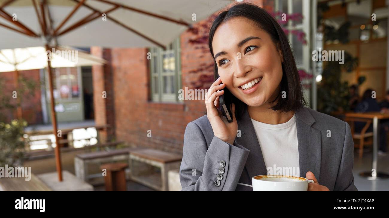 Lächelnde asiatische Geschäftsfrau, die vor dem Büro auf dem Handy telefoniert. Stockfoto