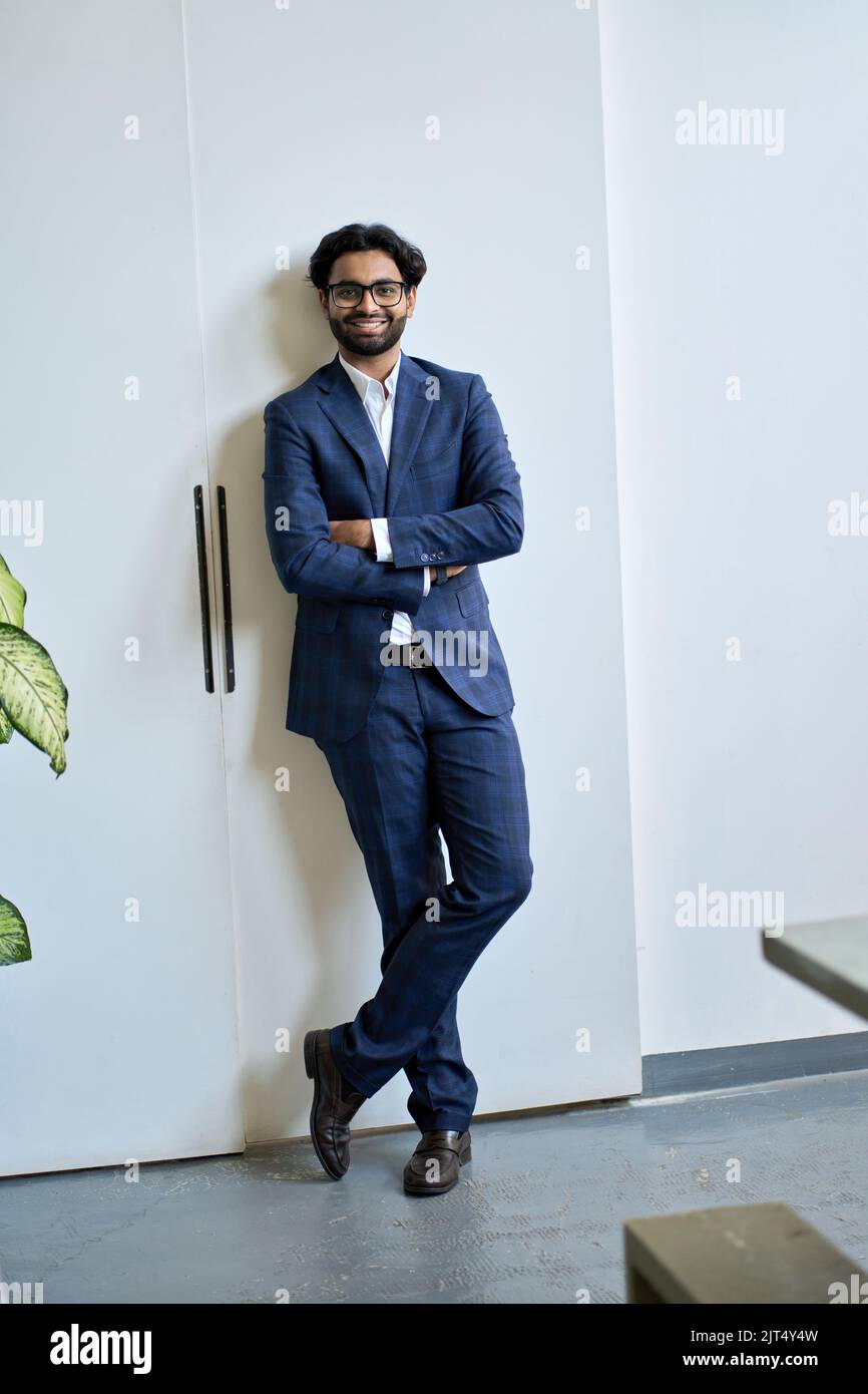 Glücklicher junger indischer Geschäftsmann trägt Anzug steht im Büro, vertikales Porträt. Stockfoto