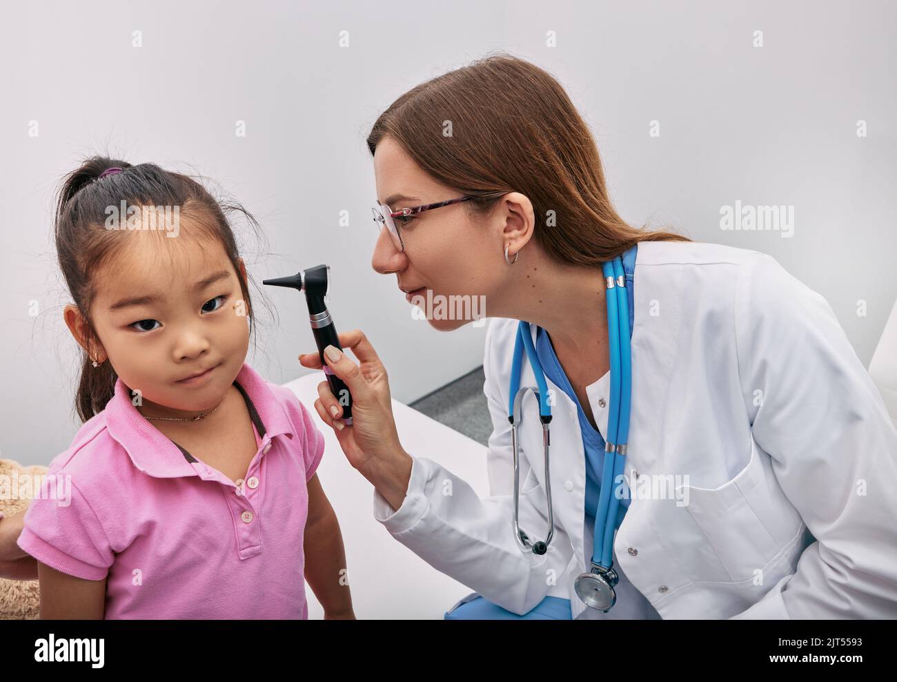 Kaukasischer Kinderarzt untersucht japanisches Mädchen mit Otoskop, Hörkontrolle für Kind. Höruntersuchung Stockfoto