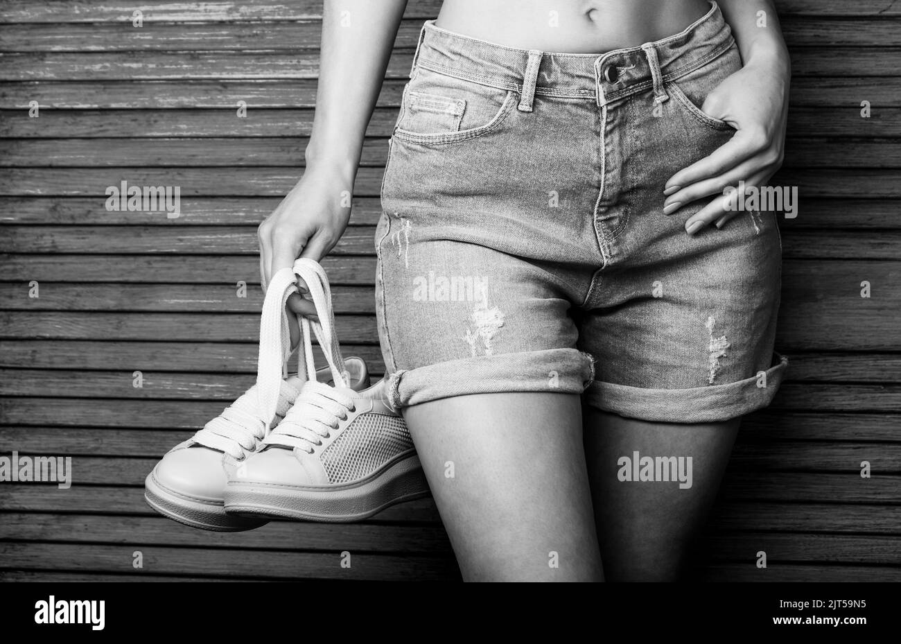 Mädchen mit einer schönen Figur in Jeans Shorts und rosa Schuhe. Frau mit Schuhen. Frau mit einem Paar rosa Schuhen. Mädchen mit einer schönen Taille in Stockfoto