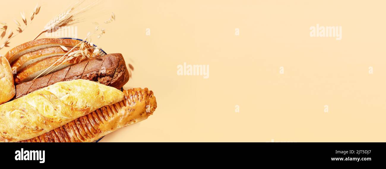 Lebensmittelbanner mit natürlichem Brot. Frisches Brot mit Roggen- und Weizenohren auf beigefarbenem Hintergrund mit Kopierfläche. Knusprige französische Baguettes, slic Stockfoto