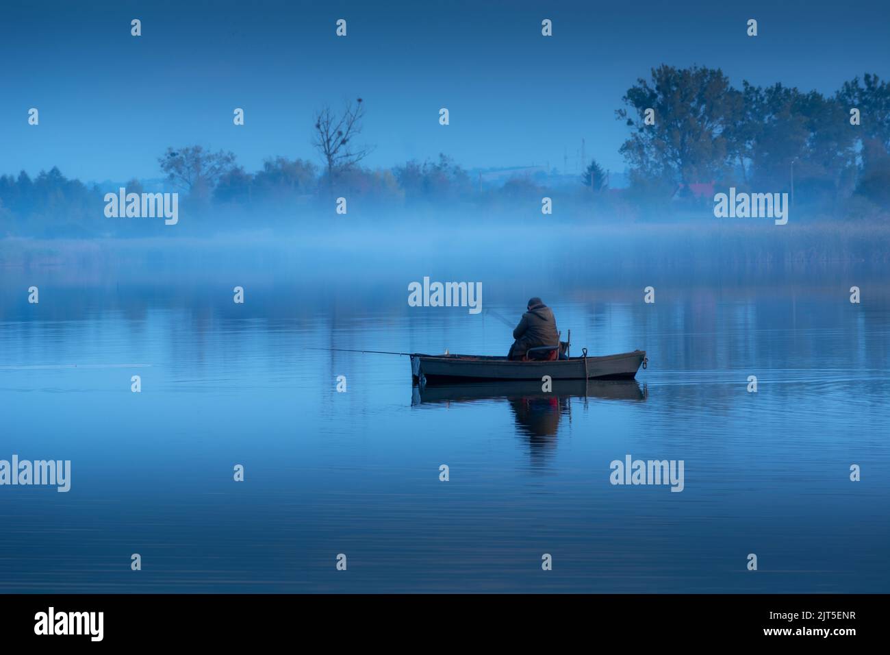 Angler in einem Boot und Nebel auf einem ruhigen See Stockfoto