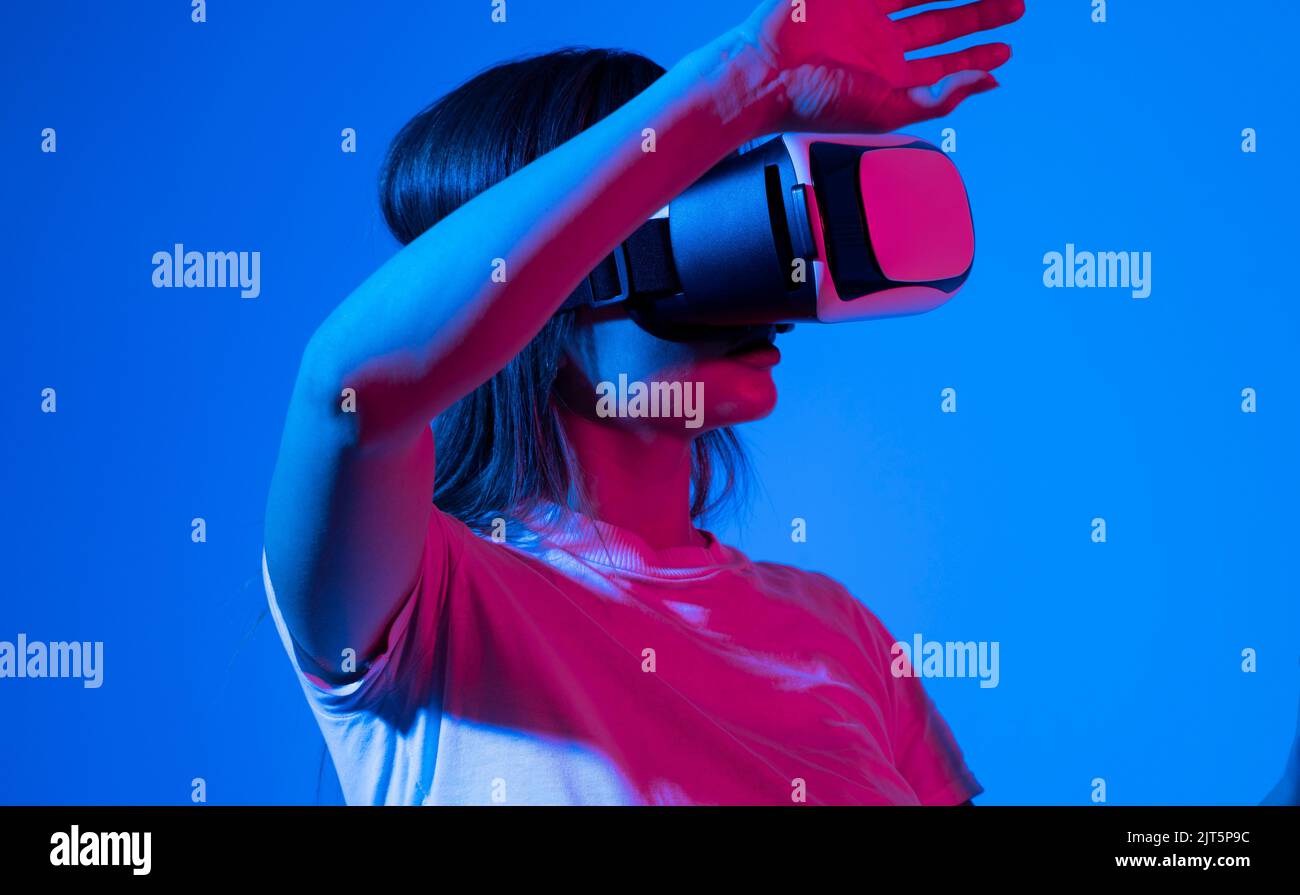 Aufgeregt Brünette Frau in weißem T-Shirt bekommen Erfahrung mit VR-Headset Brille der virtuellen Realität viel gestikulierende Hände in Neonlicht. Stockfoto