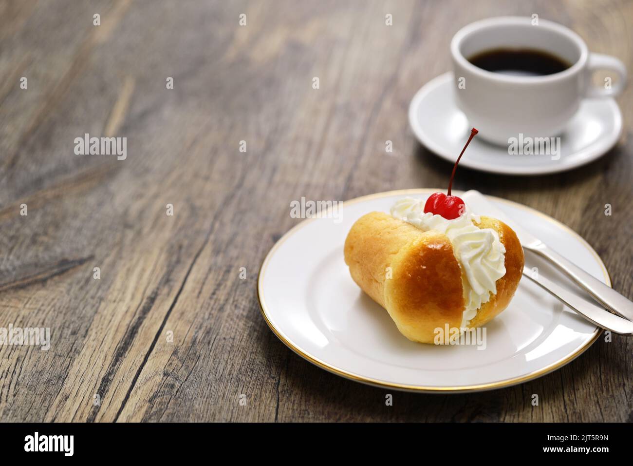 Rum baba (baba au Rhum) mit Schlagsahne dekoriert; traditionelles französisches und italienisches Dessert und eine Tasse Kaffee Stockfoto