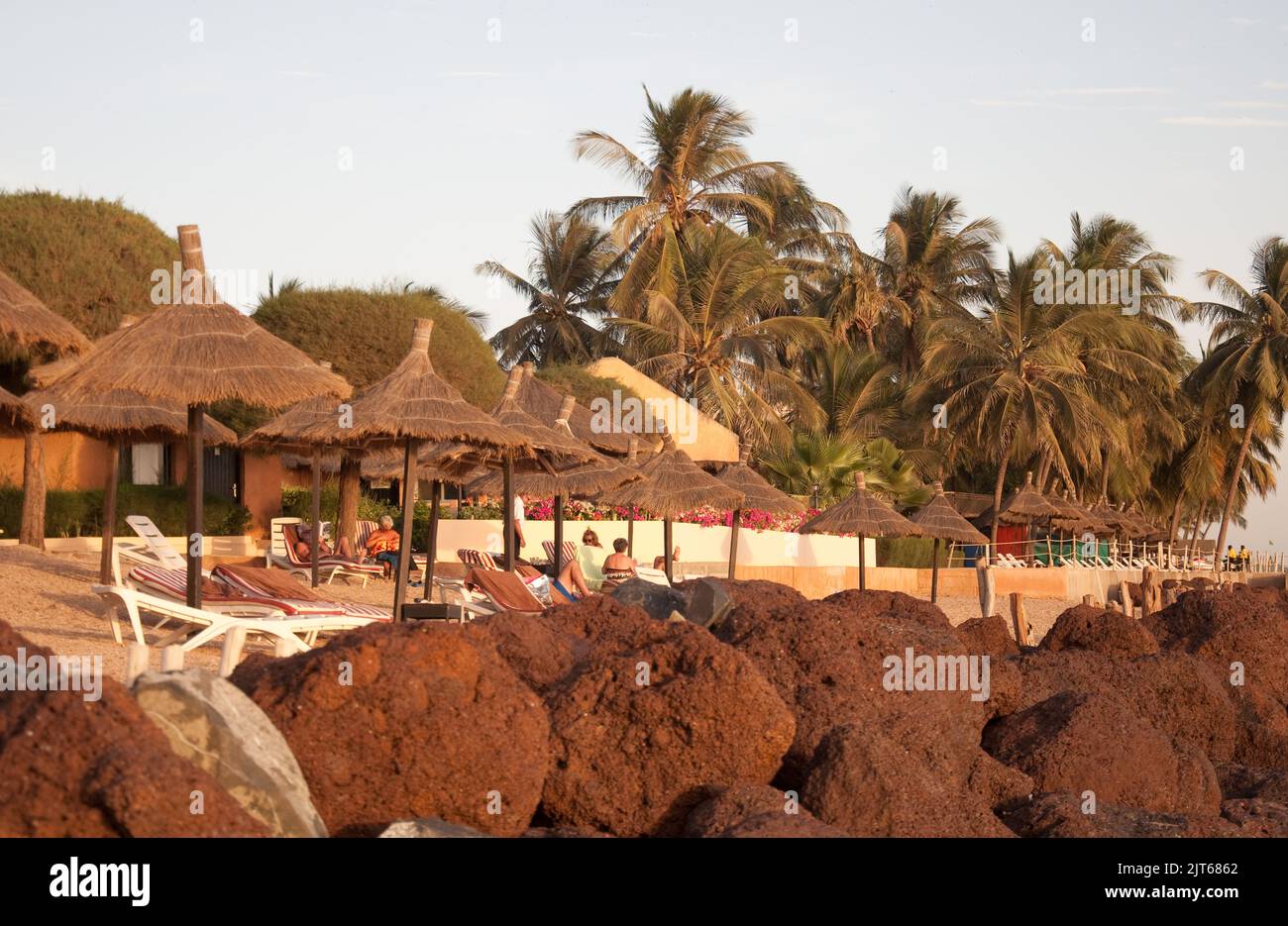 Am Strand, Saly-Portudal, Petite Côte von Senegal, Senegal. Strand, Liegestühle, Bäume, Strohdächer, Schatten am Strand, Felsen, Sonnenbaden Stockfoto