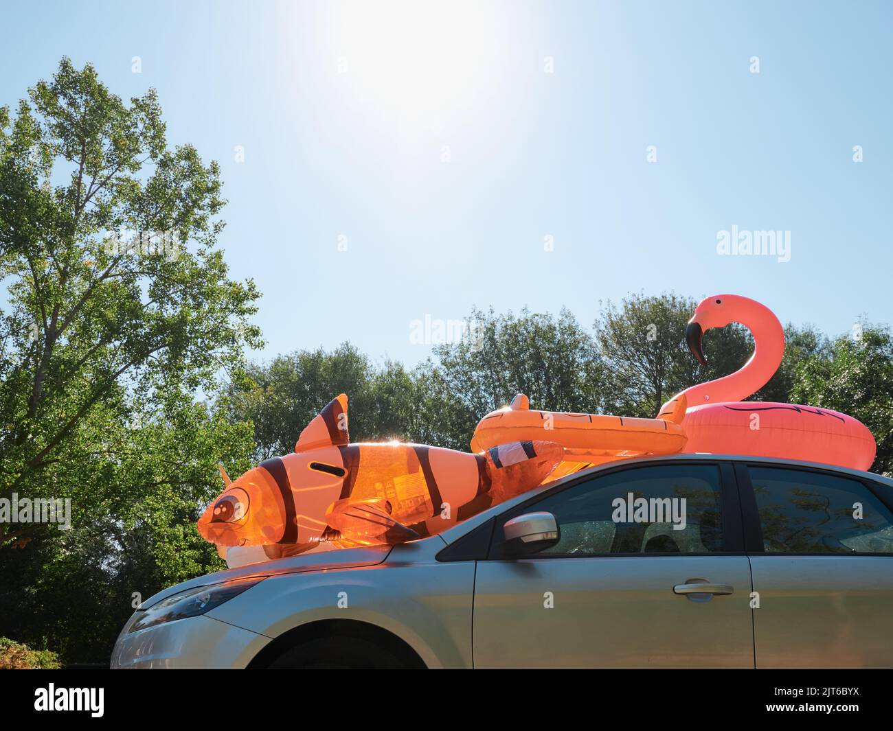 Ein Familienauto mit aufblasbarem Spielzeug für Kinder auf dem Dach in einem Sommergarkplatz - Sommer-Familienurlaubsauto packen - Sommer-Tagesauszeit - seltsam skurril Stockfoto