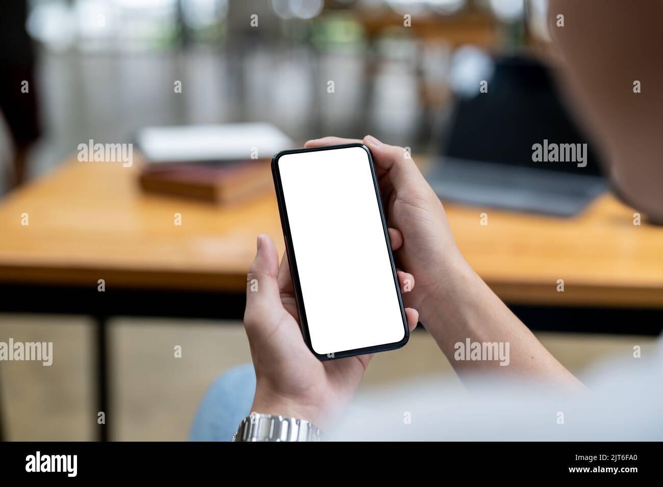 Nachbildung einer Frau, die ein schwarzes Mobiltelefon mit weißem Bildschirm hält, während sie im Café sitzt. Stockfoto