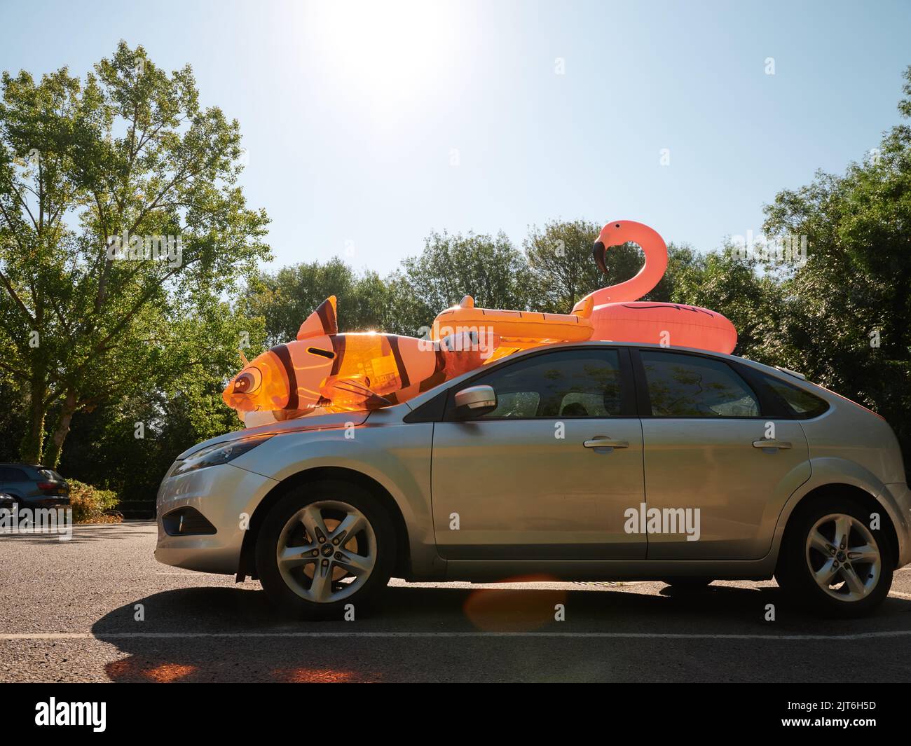 Ein Familienauto mit aufblasbarem Spielzeug für Kinder auf dem Dach in einem Sommergarkplatz - Sommer-Familienurlaubsauto packen - Sommer-Tagesauszeit - seltsam skurril Stockfoto