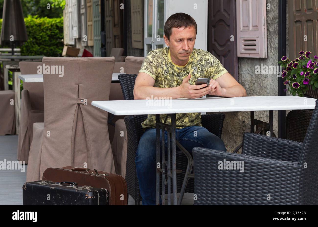 Einsam müde ernst Hipster Tourist Mann verbringt Zeit in gemütlichen Café, neben Vintage-Koffer, nachdenkliche gut aussehende Kerl in trendigen Casual Wear verwenden Gadget, Stockfoto