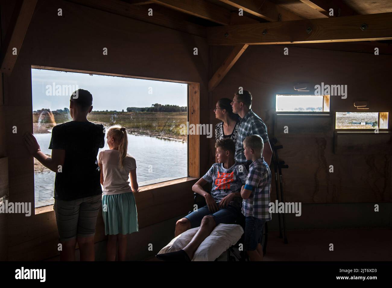 Besucher mit Jungen im Rollstuhl, die Vögel aus dem Vogelschutzgebiet von Waterdunen, Naturschutzgebiet entlang der Westschelde, Zeeland, Niederlande, betrachten Stockfoto