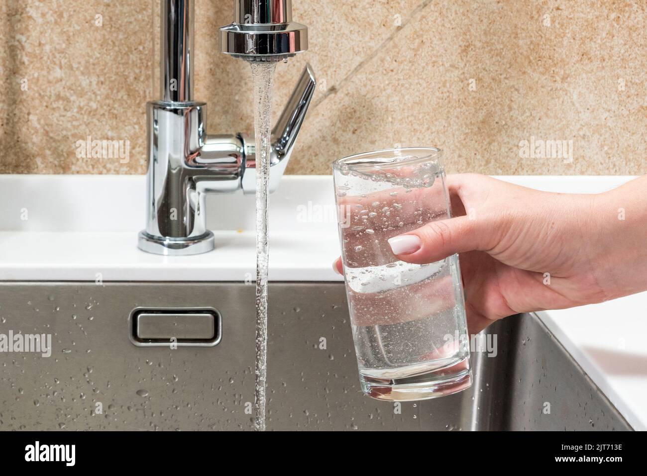 Wasser aus einem Wasserhahn in einem Glas, das von der Hand einer Frau gehalten wird Stockfoto