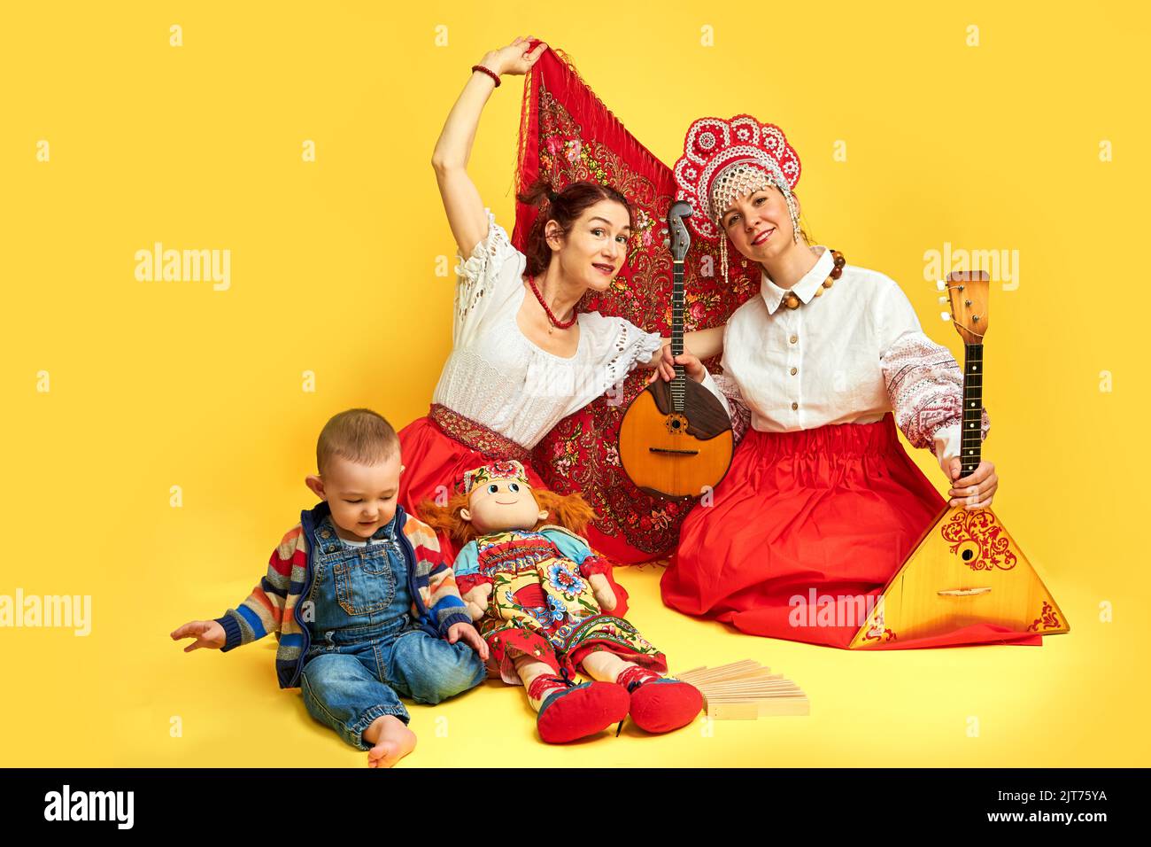 Musikerinnen in russischen Volkskleidern mit Musikinstrumenten auf gelbem Studiohintergrund. Glückliche Künstler aus Russland in Nationalkleidung mit str Stockfoto