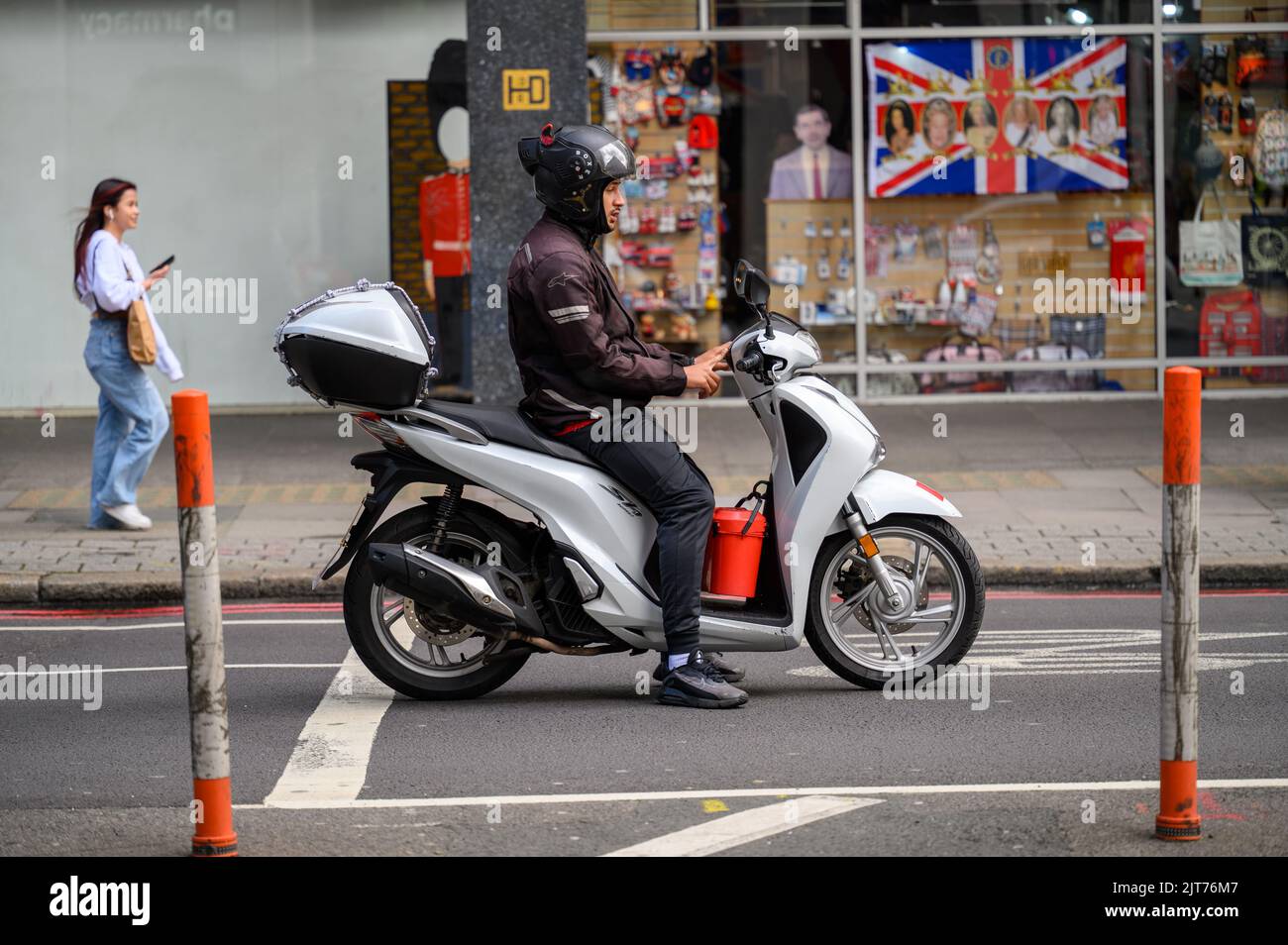 LONDON - 20. Mai 2022: Mann mit Helm auf weißem Motorroller hält auf der Straße Stockfoto
