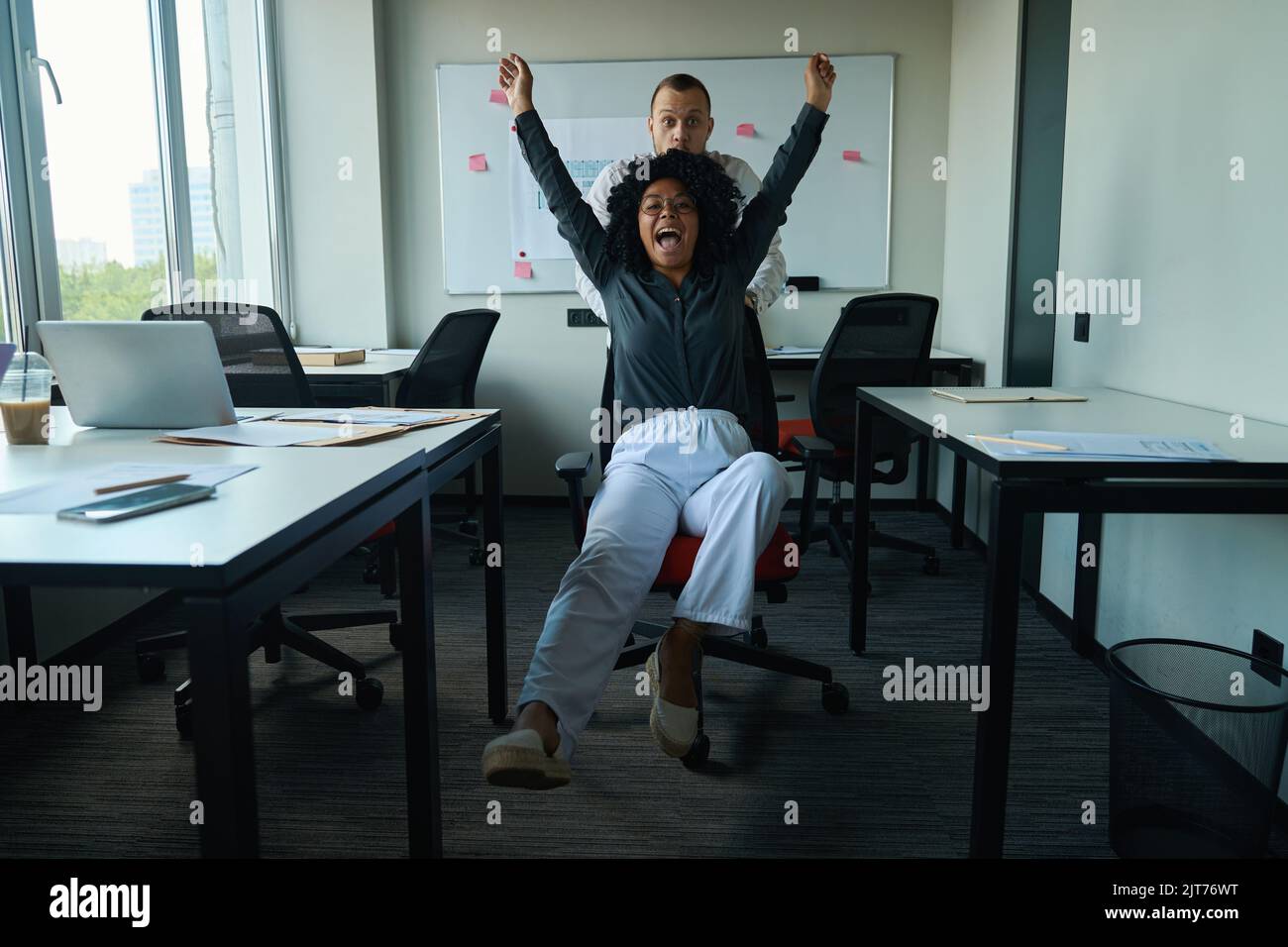 Ein Mann rollt einen glücklichen Kollegen in den Bürostuhl Stockfoto