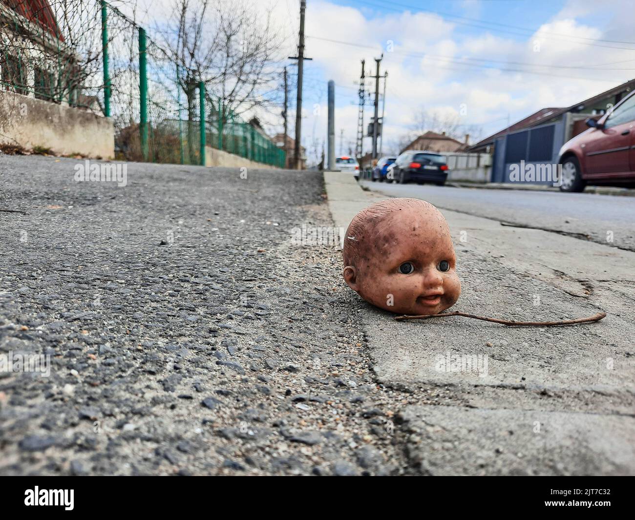 Ein Puppenkopf ohne Körper, der auf der Straße sitzt. Kinderspielzeug. Stockfoto