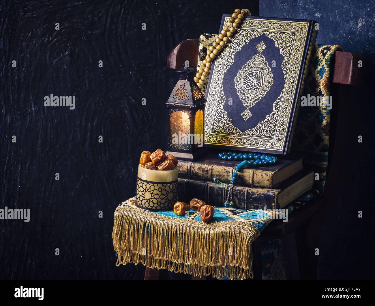 Das islamische Heilige Buch 'Quran' ist mit Rosenkranz, orientalischer Ramadan-Laterne, frischen Datteln und einem Gebetsteppich auf einem Holzstuhl platziert. Stockfoto