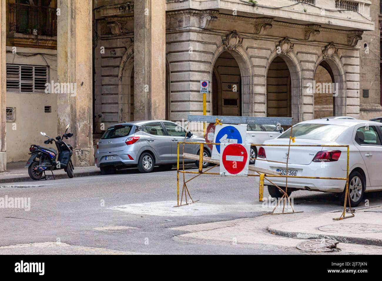 Moderne Autos werden in einer Stadtstraße geparkt, wo verwitterte Gebäude mit republikanischer Architektur stehen. Es gibt zwei metallische Barrieren mit Stockfoto