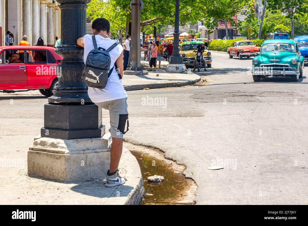 Ein junger Mann lehnt sich an den Pol einer Straßenlaternen. Ein Oldtimer fährt in die Innenstadt. Schmutziges Wasser stagniert auf dem Bürgersteig Stockfoto