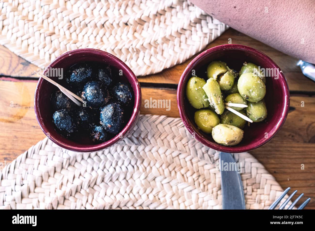 Grüne und schwarze Oliven mit Gewürzen, serviert auf brauner Keramik als Gurken auf einem Restauranttisch Stockfoto