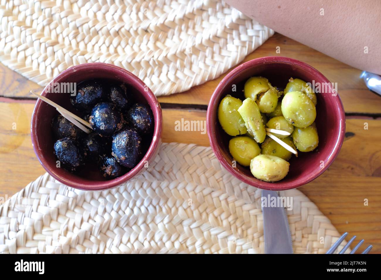 Grüne und schwarze Oliven mit Gewürzen, serviert auf brauner Keramik als Gurken auf einem Restauranttisch Stockfoto