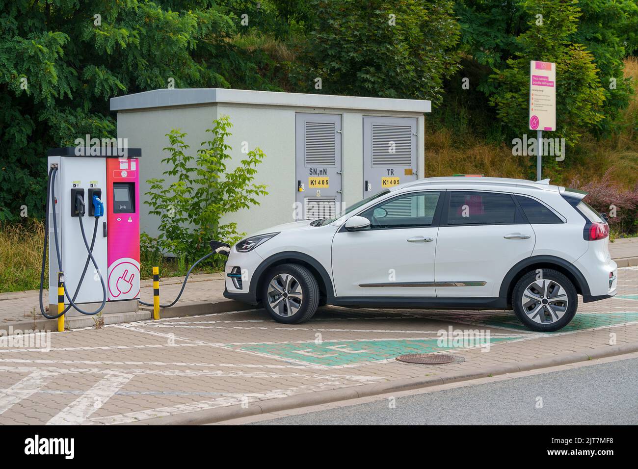 Ein weißes Elektroauto, das an eine Ladestation angeschlossen ist, um seine Batterien auf einem Parkplatz in der Nähe der Straße aufzuladen. Elektrofahrzeug, Crossover, EV Stockfoto