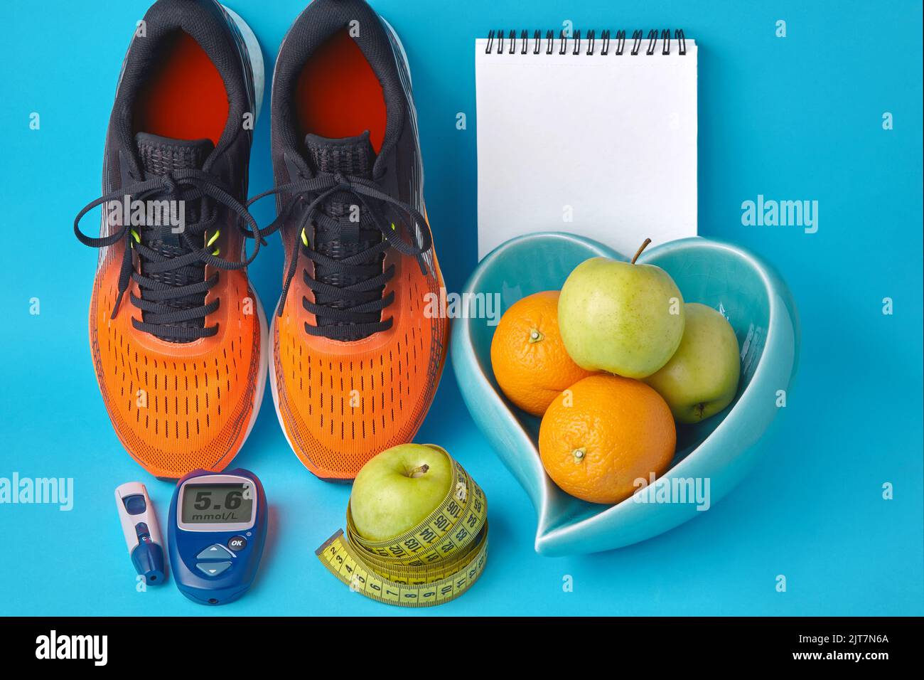 Orangefarbene Turnschuhe, Tagebuch-Notizbuch, Glucometer, Maßband und Früchte auf blauem Hintergrund Stockfoto