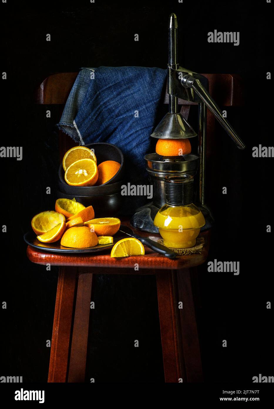 Orangensaftflasche mit alter traditioneller Quetschpresse und frischen Orangen auf Holzstuhl. Stockfoto