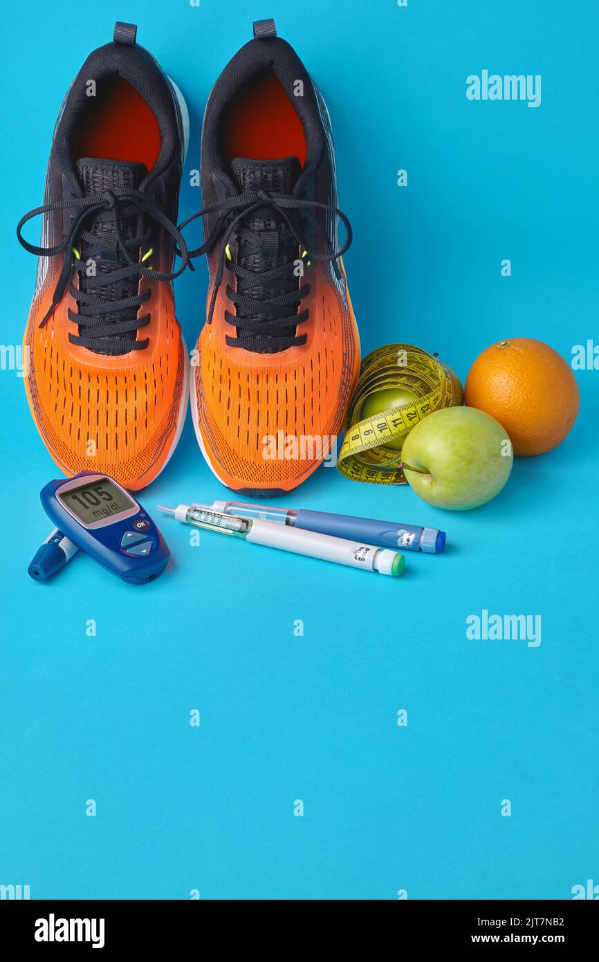 Orangefarbene Sneakers, Früchte, Maßband, Glucometer und Insulin-Spritzenstifte auf blauem Hintergrund Stockfoto