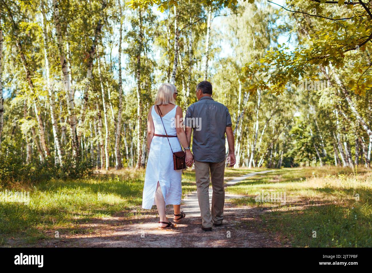 Ältere Familienpaare, die im Sommerwald im Freien spazieren. Ältere Menschen halten sich die Hände. Romantisches Date Stockfoto