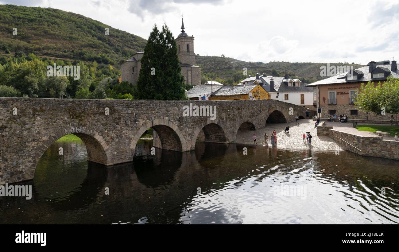 Besucher genießen den Fluss Meruelo mit der berühmten römischen Brücke im Dorf Molinaseca entlang des Camino Frances in León, Spanien. Dieses alte rou Stockfoto